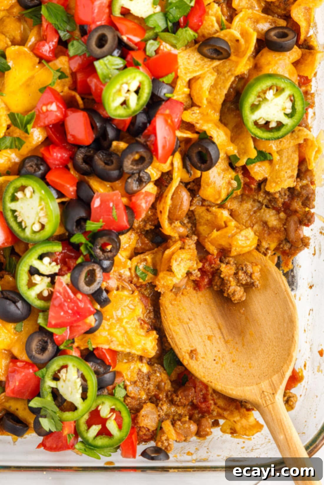 Crunchy Chili Cheese Delight 2 A spoon scooping a generous portion of Frito Pie casserole, showcasing layers of seasoned beef, melted cheese, and golden Frito chips.