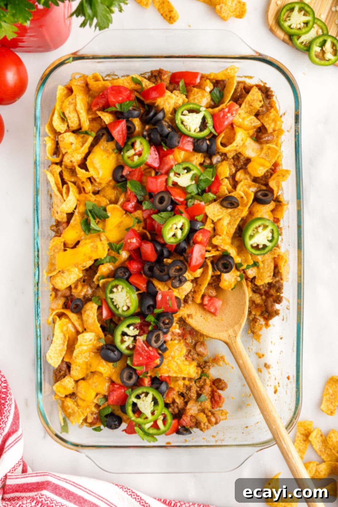 Crunchy Chili Cheese Delight 13 A Frito Pie casserole serving, with a wooden spoon inserted, showing the rich, cheesy, and meaty layers ready to be enjoyed.