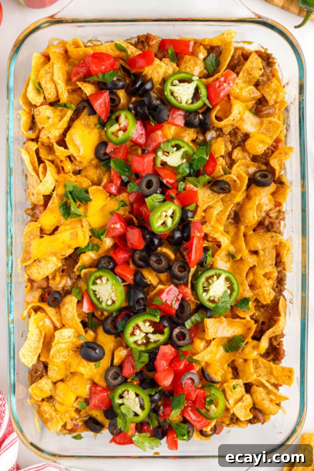 Crunchy Chili Cheese Delight 3 An overhead shot of a baked Frito Pie casserole, showing a golden brown crust of cheese and Frito chips, with colorful garnishes.