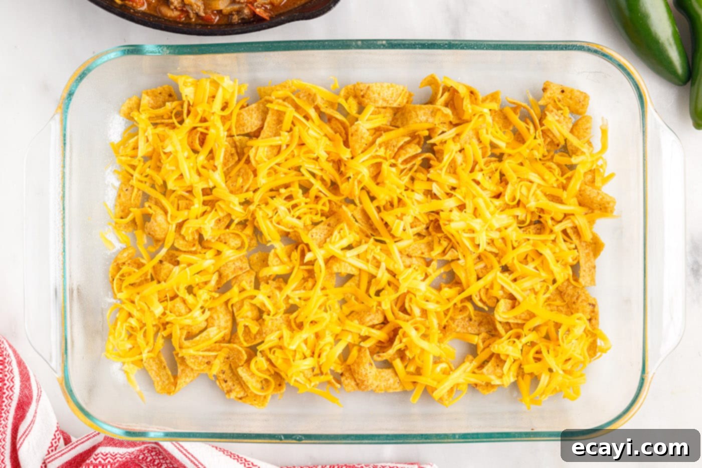 Crunchy Chili Cheese Delight 8 Half of the Frito corn chips spread at the bottom of a casserole dish, topped with a layer of shredded cheese.