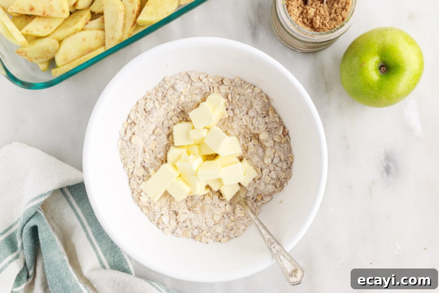 Warm Apple Crumble Delight 8 Cold, cubed butter pieces scattered over a mixture of rolled oats, flour, and brown sugar in a mixing bowl.