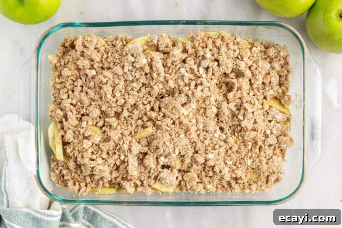 Warm Apple Crumble Delight 10 The buttery oat crumble topping sprinkled generously over the spiced apple filling in the baking dish, ready for the oven.