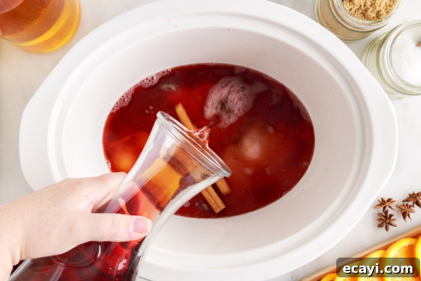 Mulled Cranberry Cheer 6 pouring juices into hot cranberry punch in the crockpot