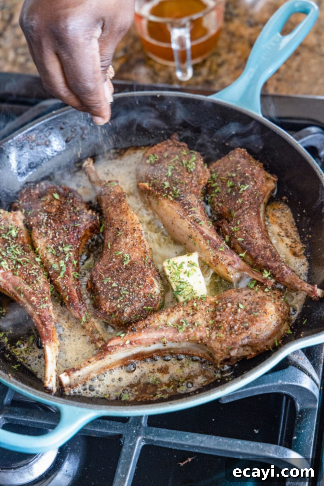 Gourmet Lamb Lollipops 2 Close-up of pan-seared lollipop lamb chops being sprinkled with fresh thyme in a skillet, showcasing the golden brown crust.