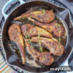 Gourmet Lamb Lollipops 10 A close-up view of perfectly pan-seared Lollipop Lamb Chops resting in a skillet, glistening with butter and thyme.