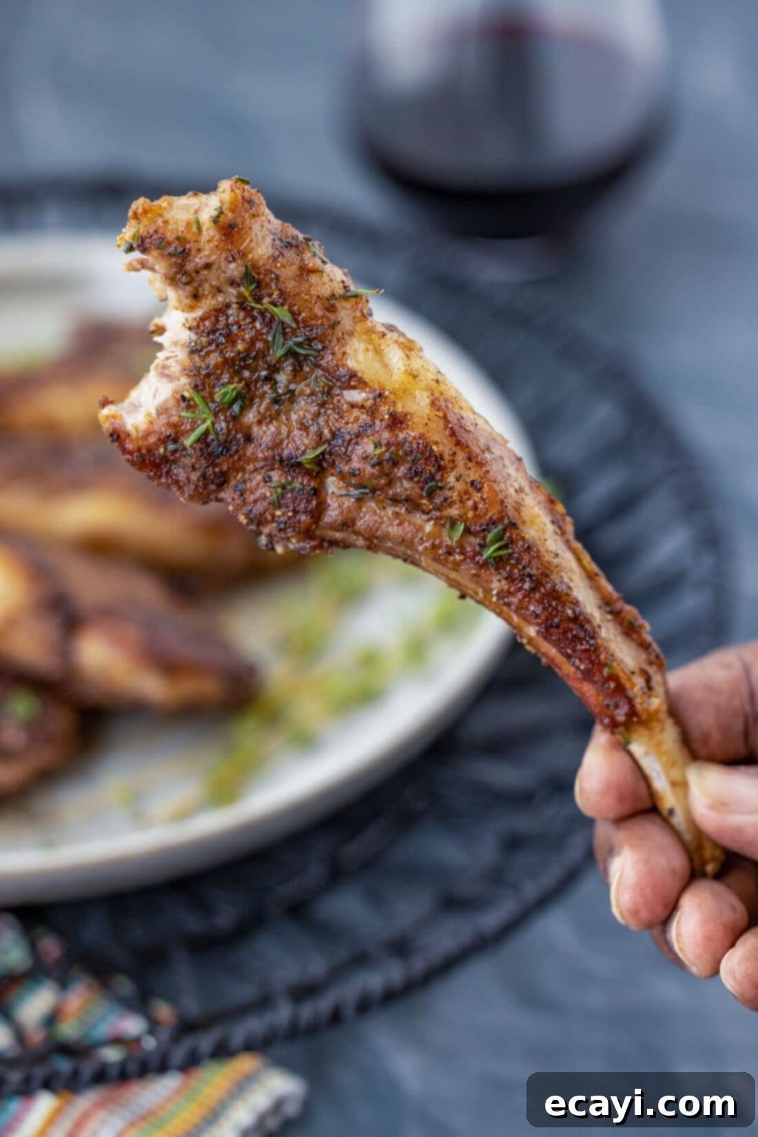 Gourmet Lamb Lollipops 9 A hand holding a perfectly cooked lollipop lamb chop by the bone, showcasing its tender meat and crispy crust.