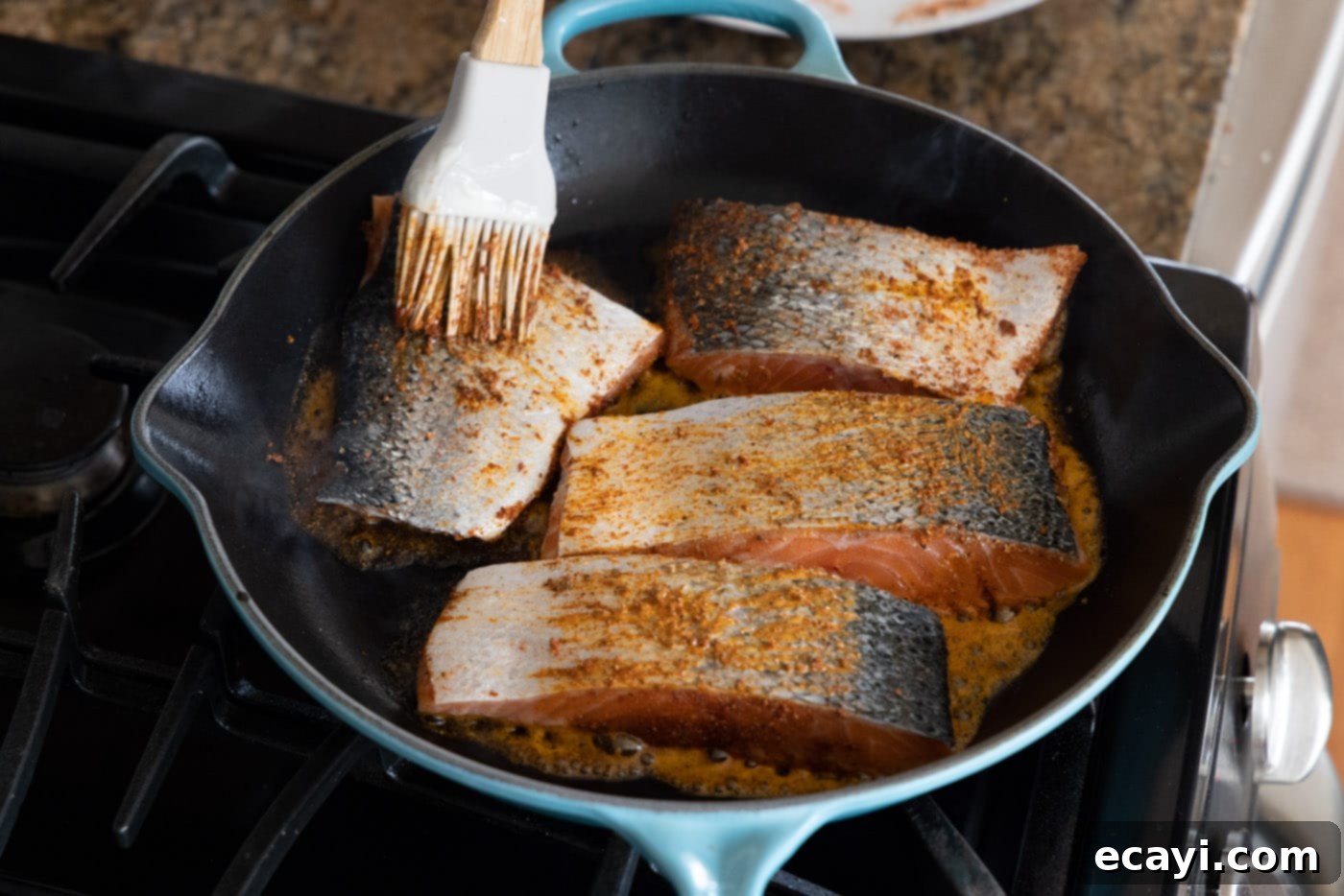 Cajun Seared Salmon 9 The skin side of salmon fillets being brushed with butter and seasoning mixture while cooking in the skillet.