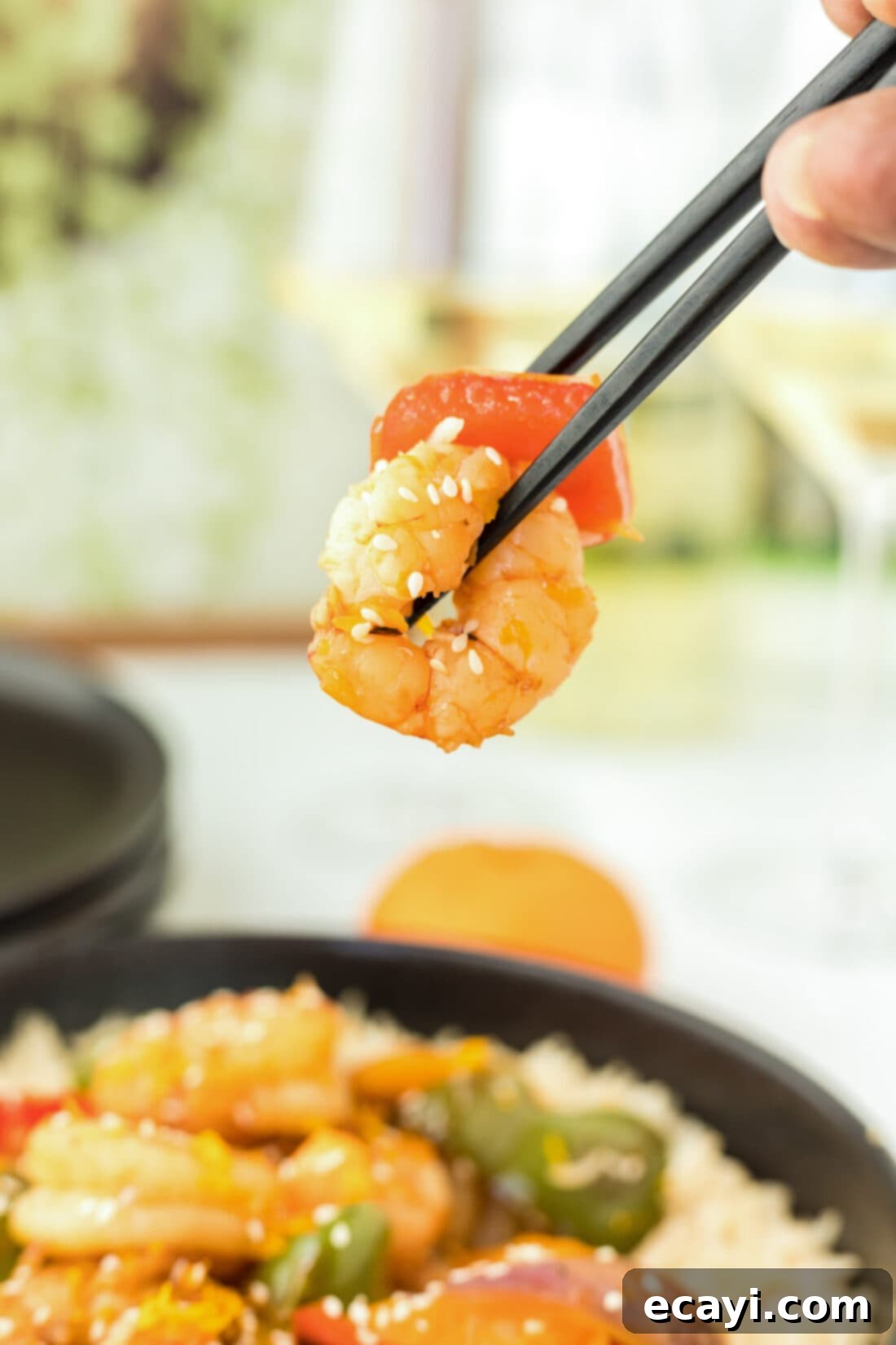 Zesty Peppercorn Shrimp 16 A pair of chopsticks lifting a piece of Citrus Pepper Shrimp, highlighting the glossy sauce and cooked vegetables.
