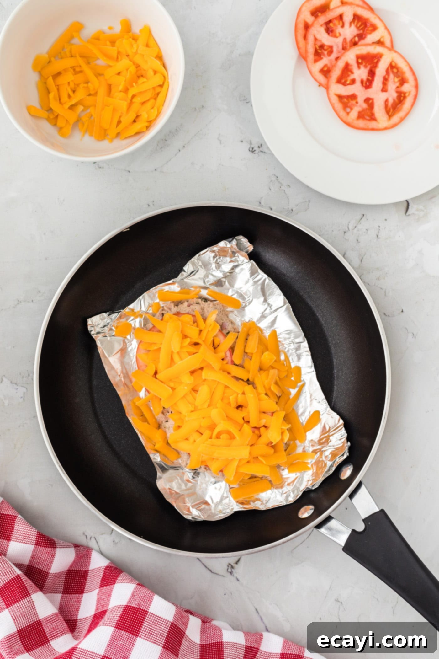 Golden Tuna Grille 7 Shredded cheddar cheese layered over fresh tomato slices and tuna salad in a foil bowl.