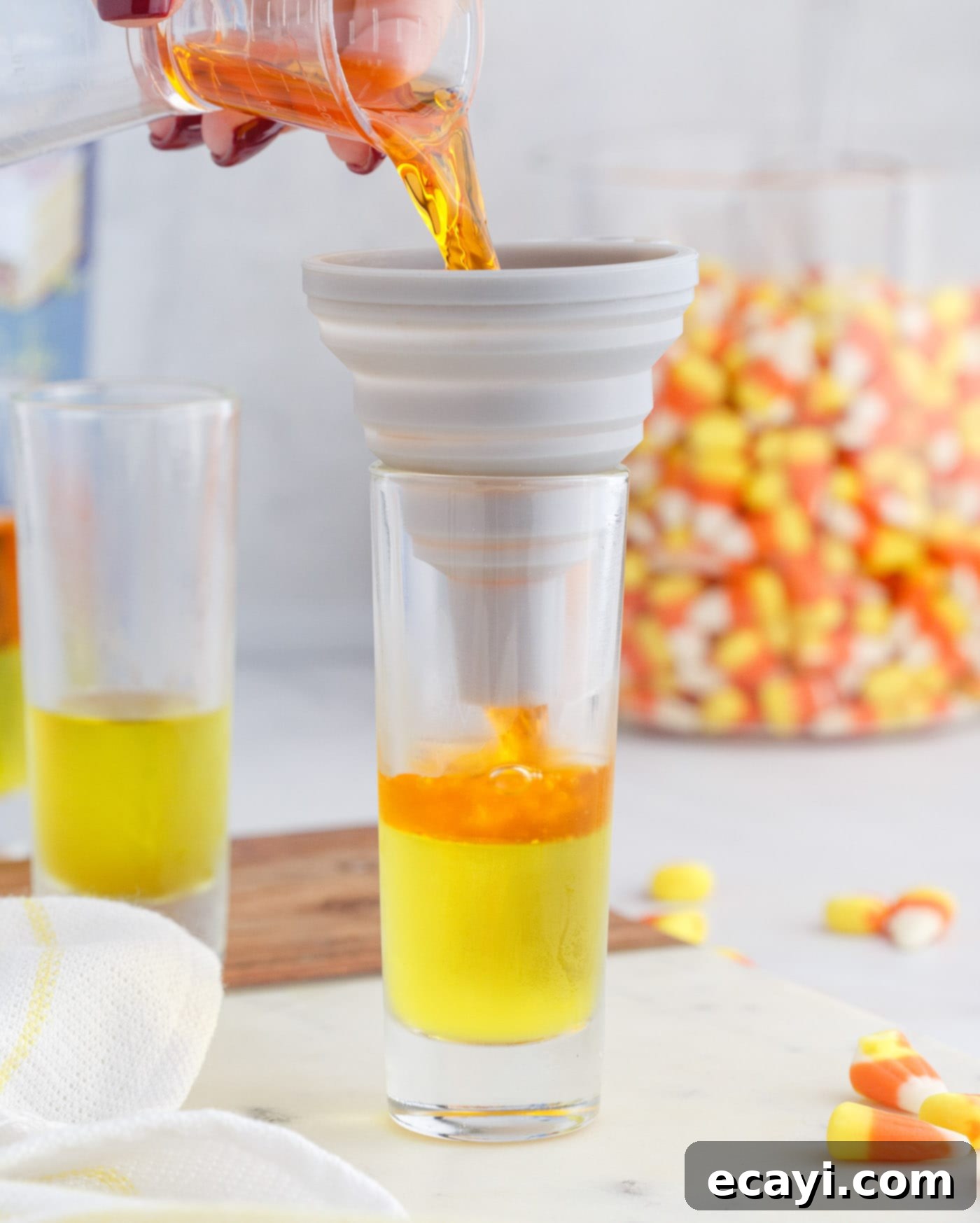 Harvest Hues Shooters 8 pouring orange jello mix over the top of lemon jello in a shot glass
