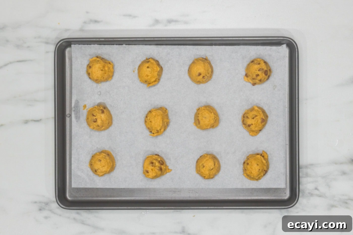 Spiced Pumpkin Cinnamon Chip Cookies 11 Uniform balls of pumpkin cinnamon chip cookie dough neatly arranged on a parchment-lined baking sheet, spaced for optimal baking.