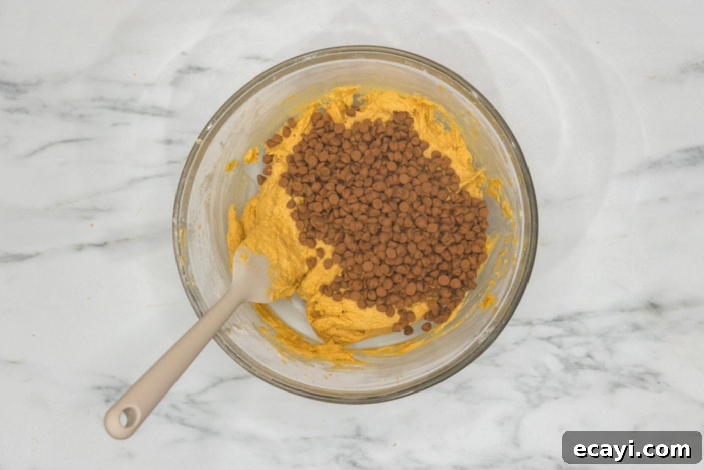 Spiced Pumpkin Cinnamon Chip Cookies 10 Cinnamon chips being gently folded into a bowl of pumpkin cookie dough with a wooden spoon.
