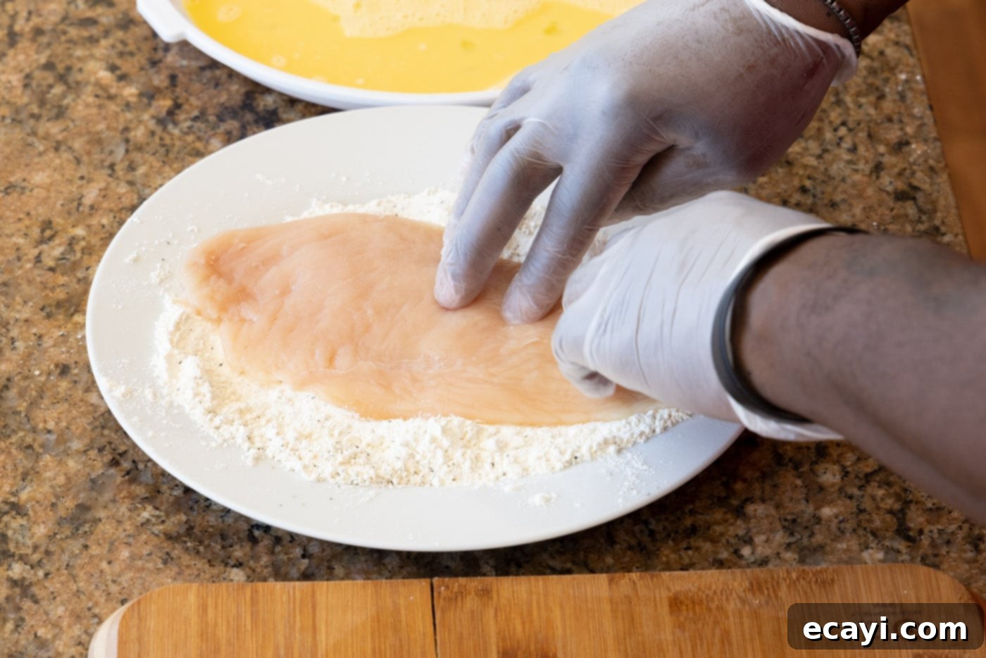 Crispy Chicken Milanese 8 Hand pressing a chicken cutlet into flour mixture, ensuring full coverage