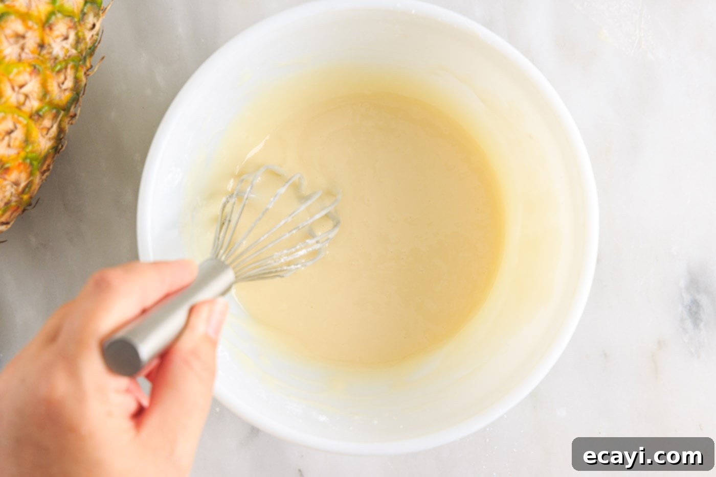 Sunshine Pineapple Pound Cake 12 Ingredients for the pineapple vanilla glaze being whisked together in a bowl until smooth.