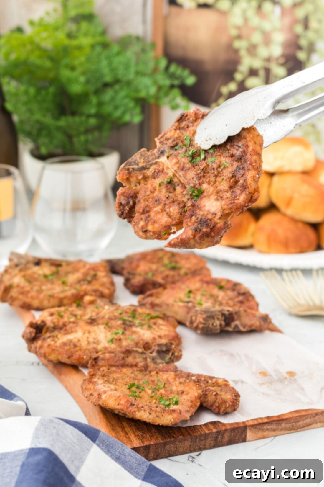 Golden Crispy Pork Chops 3 Tongs lifting a perfectly pan-fried pork chop from a skillet