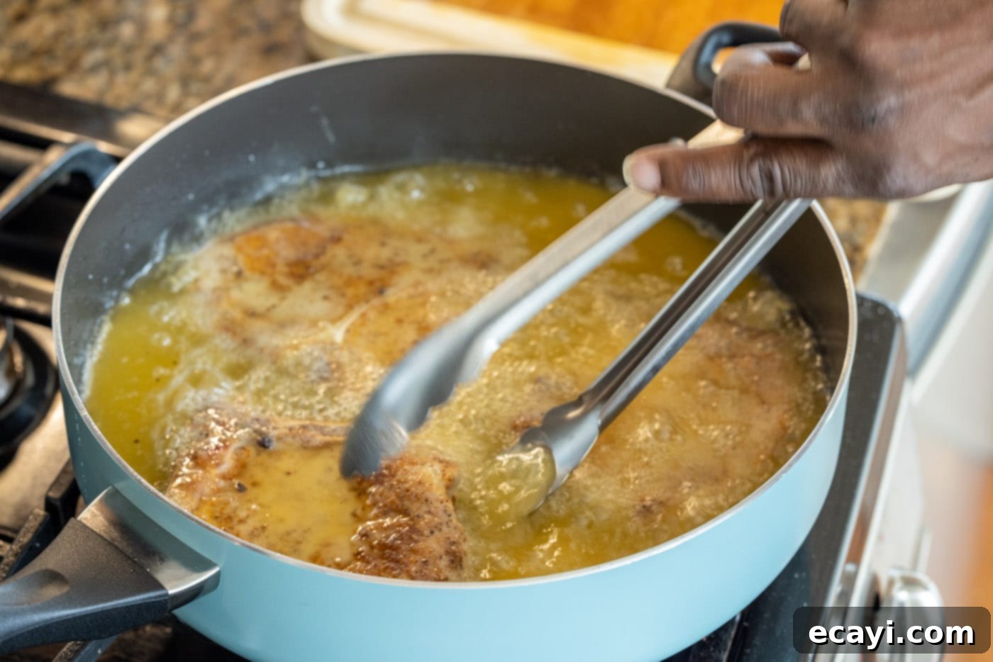 Golden Crispy Pork Chops 9 Tongs flipping a frying pork chop in a skillet, revealing a golden-brown crust