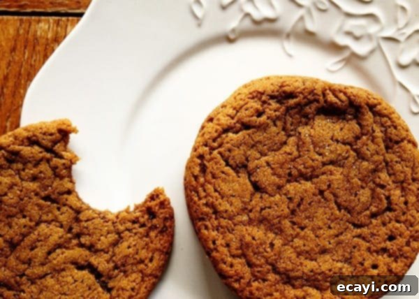 Sugar Topped Molasses Spice Cookies - AmandasCookin.com A close up photo of a whole sugar topped molasses spice cookie next to a half eaten cookie on a white plate.
