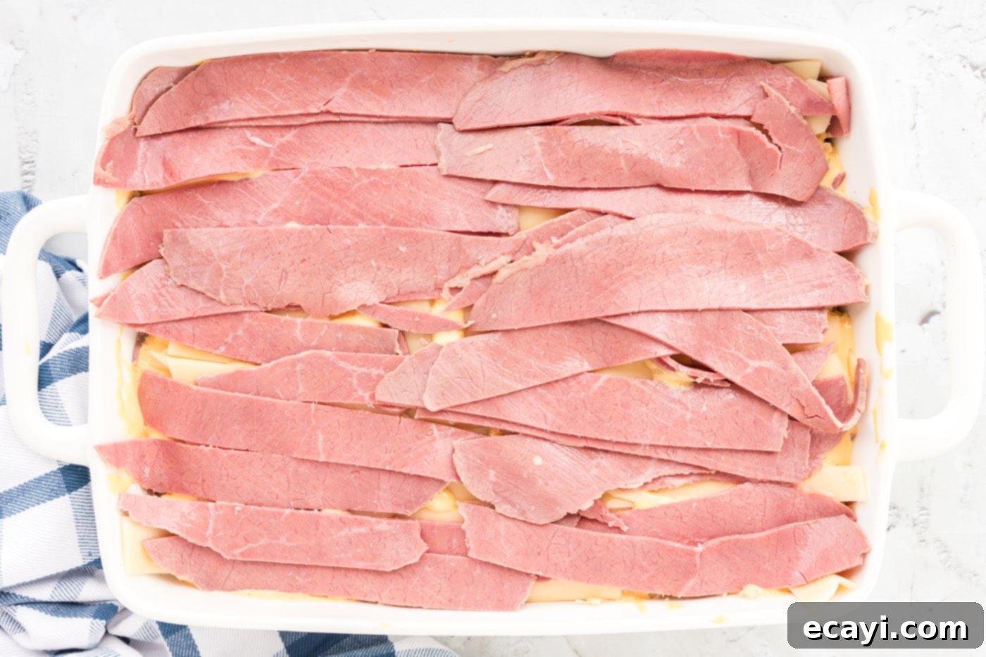 Ultimate Reuben Casserole Bake 14 A second layer of corned beef strips being added to the Reuben casserole in the baking dish.