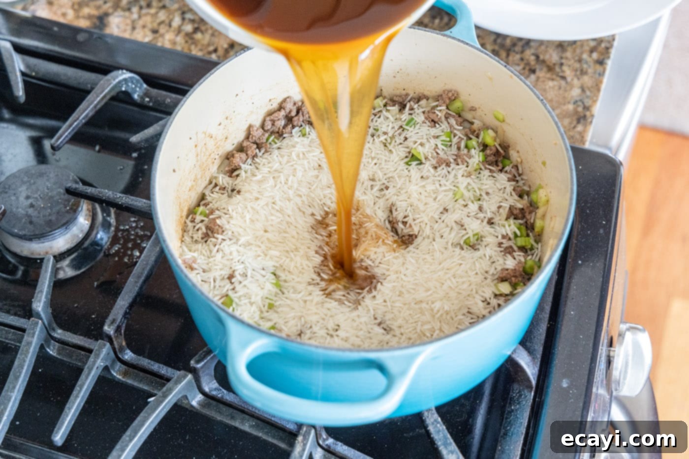 Soulful Louisiana Rice 9 Pouring beef broth over the dirty rice mixture in a Dutch oven.