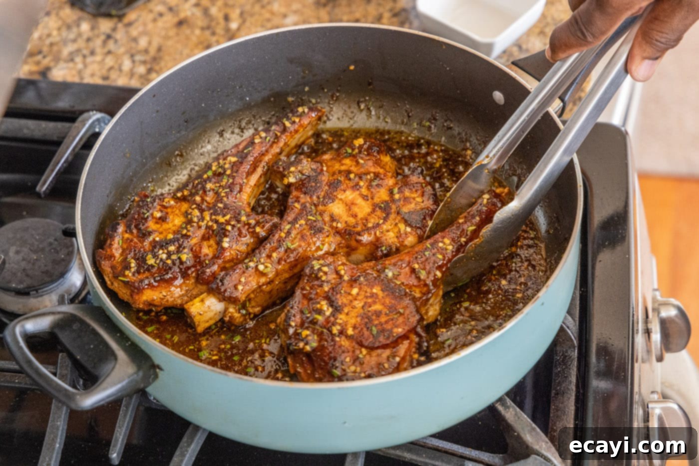 Succulent Veal Chops 14 Tongs flipping a veal chop in the pan, ensuring it's fully coated in the glistening rosemary, lemon, and garlic sauce.
