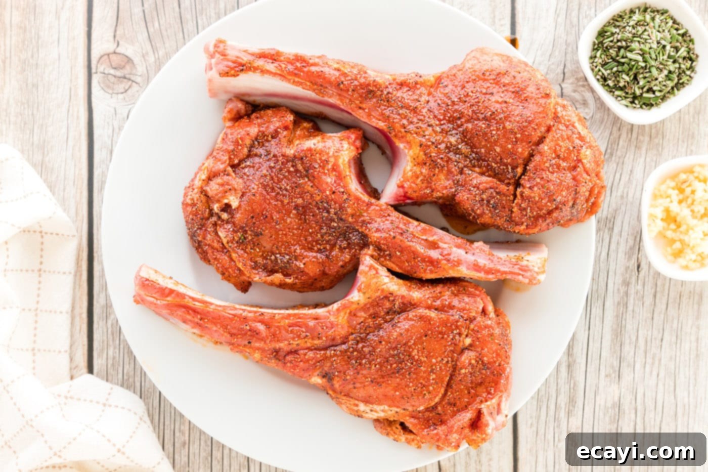 Succulent Veal Chops 6 Three raw veal chops heavily coated with a rich, dark spice rub, ready for searing.