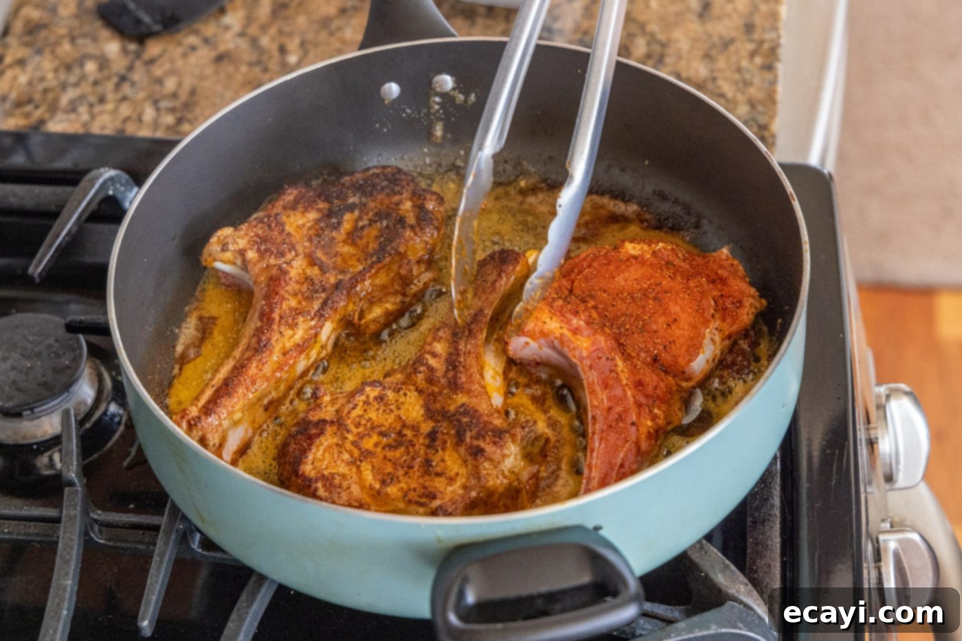 Succulent Veal Chops 8 A hand using tongs to carefully flip a pan-seared veal chop in a hot skillet, revealing its perfectly browned side.