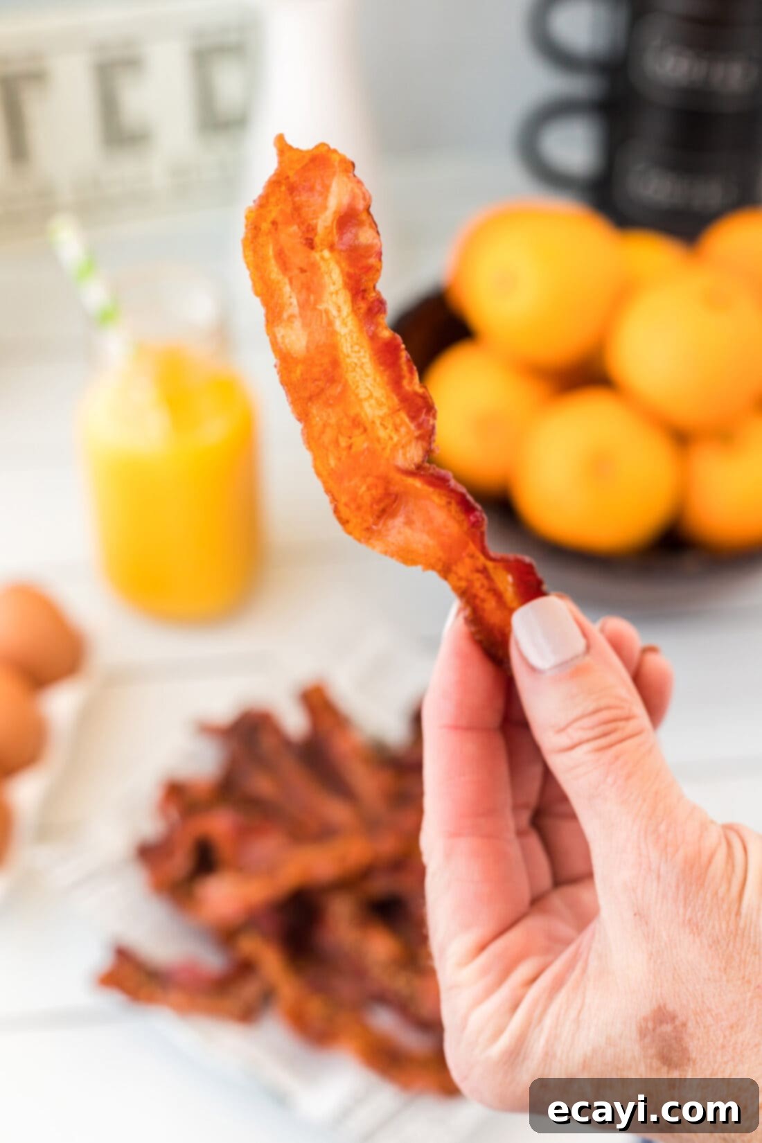 Perfect Crispy Oven Bacon 2 A hand holding a piece of perfectly crispy, golden-brown oven-baked bacon