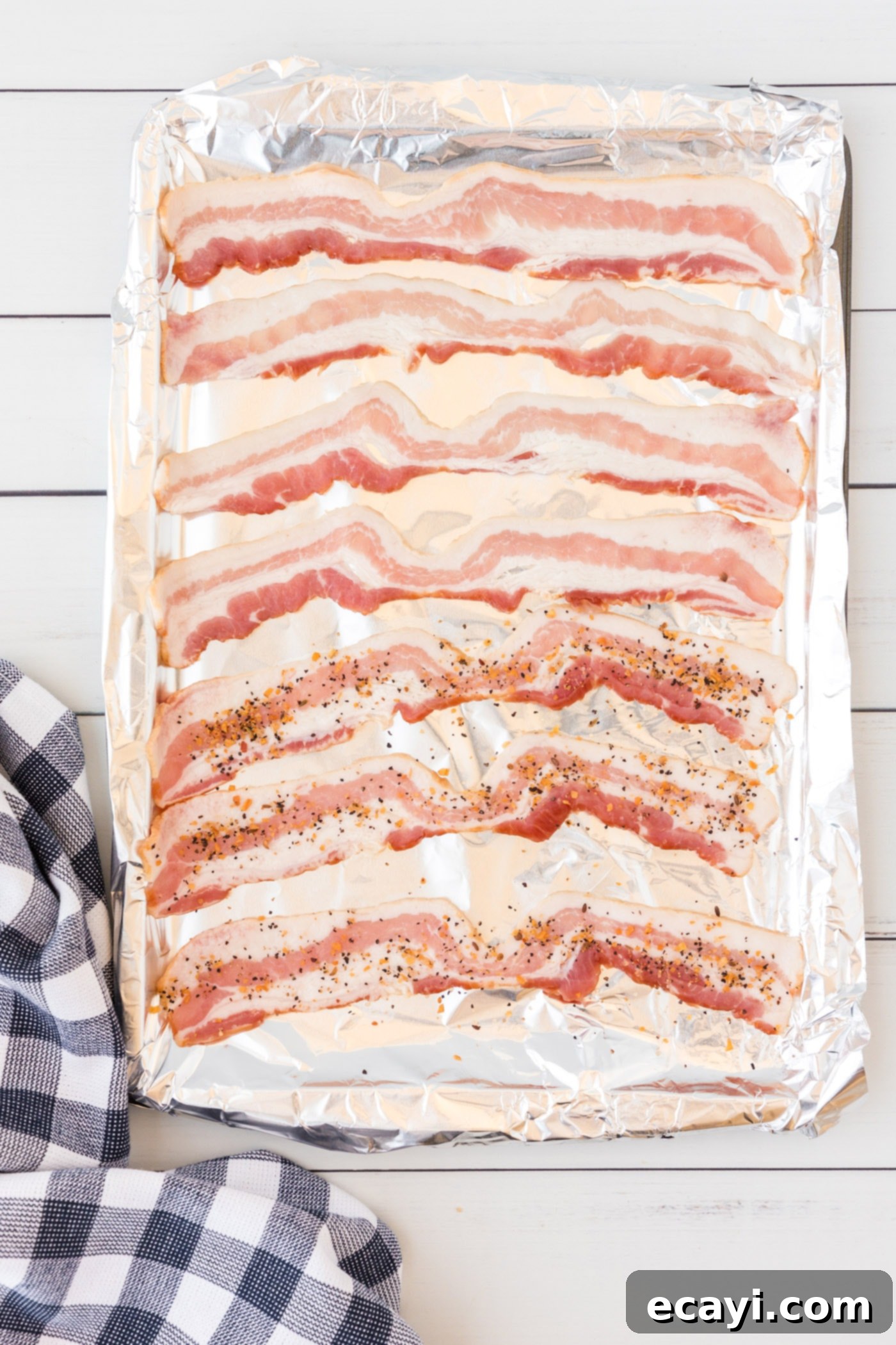 Perfect Crispy Oven Bacon 5 Raw bacon slices arranged in a single layer on a foil-lined baking sheet, lightly seasoned with Montreal Steak Seasoning