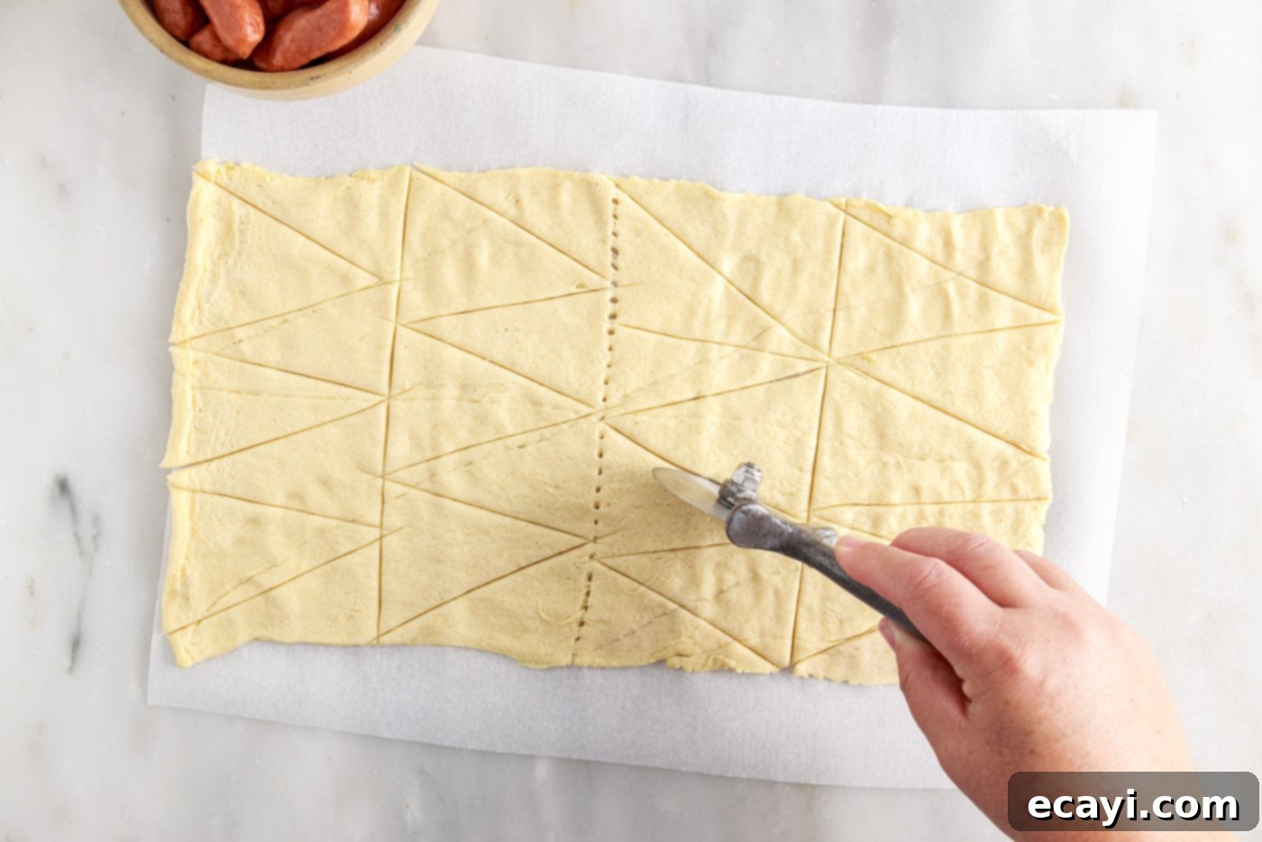 Swaddled Sausages 5 slicing crescent roll dough into triangles with a pizza wheel