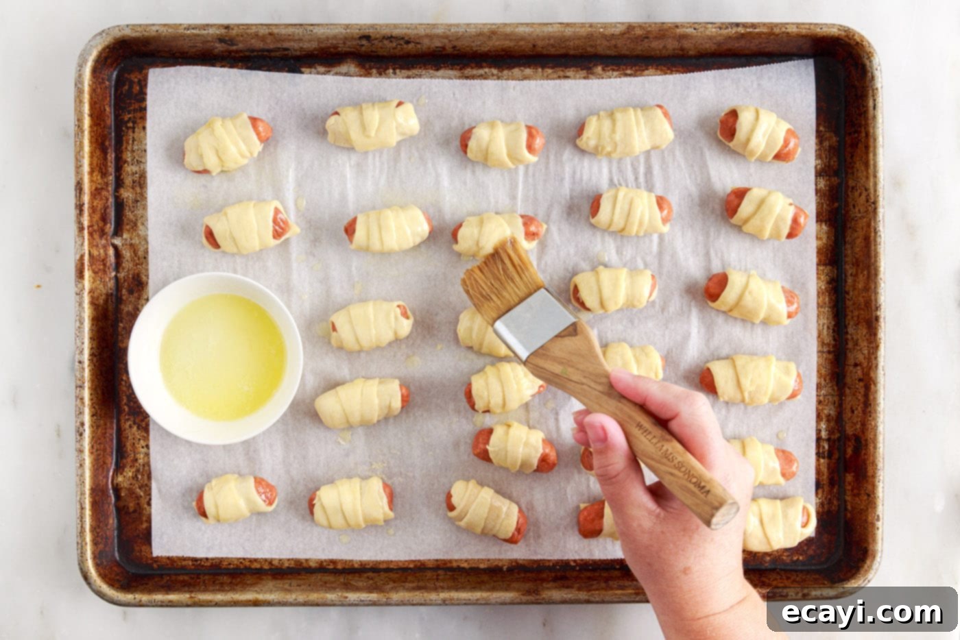 Swaddled Sausages 9 brushing pigs in a blanket with melted butter on a baking sheet