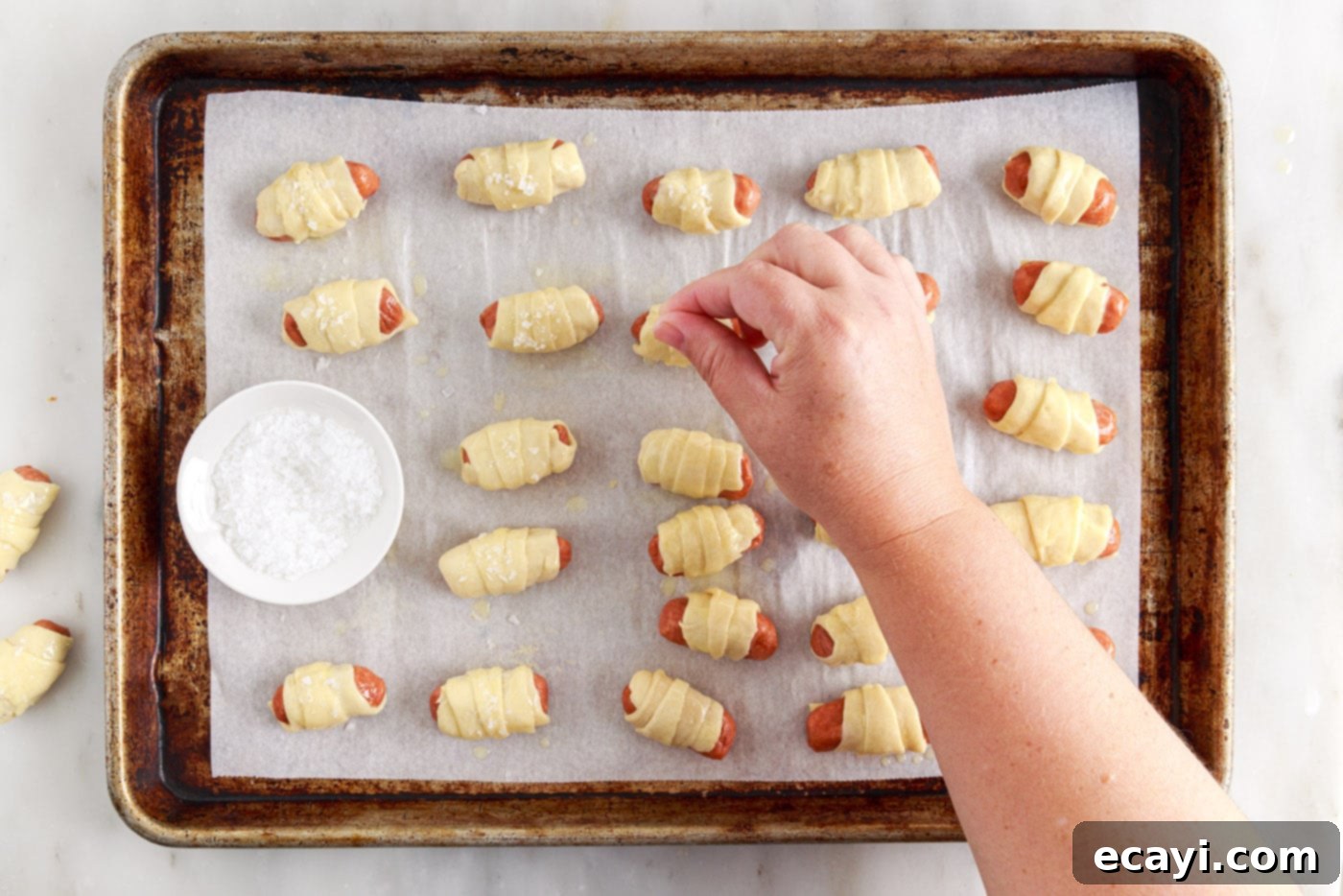 Swaddled Sausages 10 hand sprinkling flaked salt over buttered pigs in a blanket