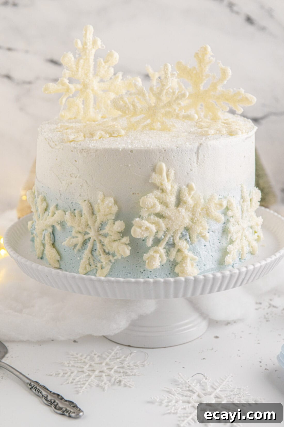 Crystalline Dream Cake 2 Snowflake Cake on a cake plate, adorned with white chocolate snowflakes and ombre blue and white frosting.