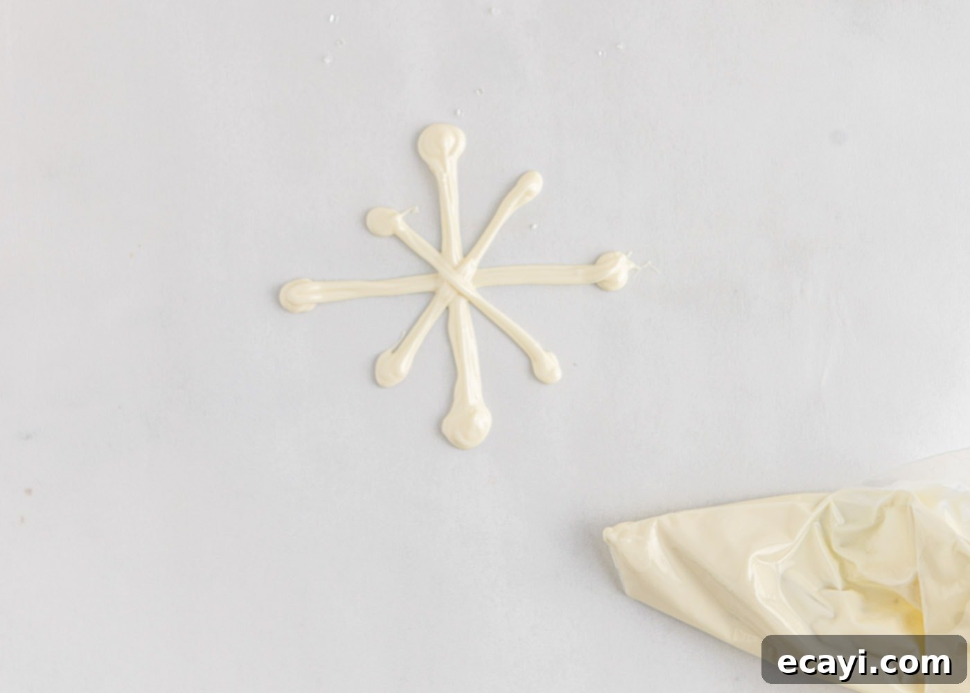 Crystalline Dream Cake 11 Piping a white chocolate snowflake design onto parchment paper.