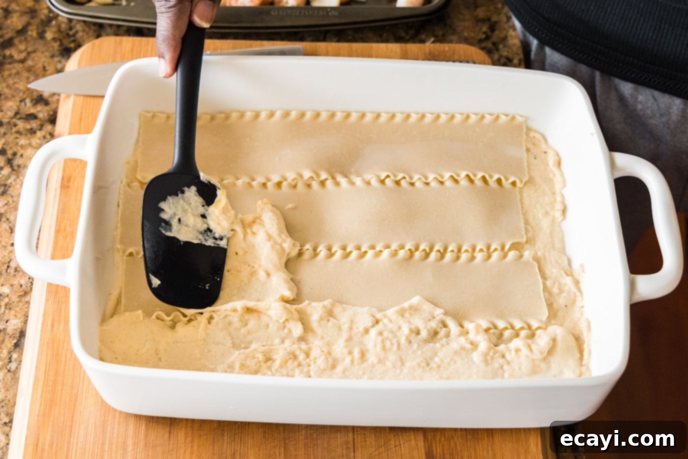 Ocean's Bounty Lasagna 17 Spreading a layer of cream sauce on top of the lasagna noodles.