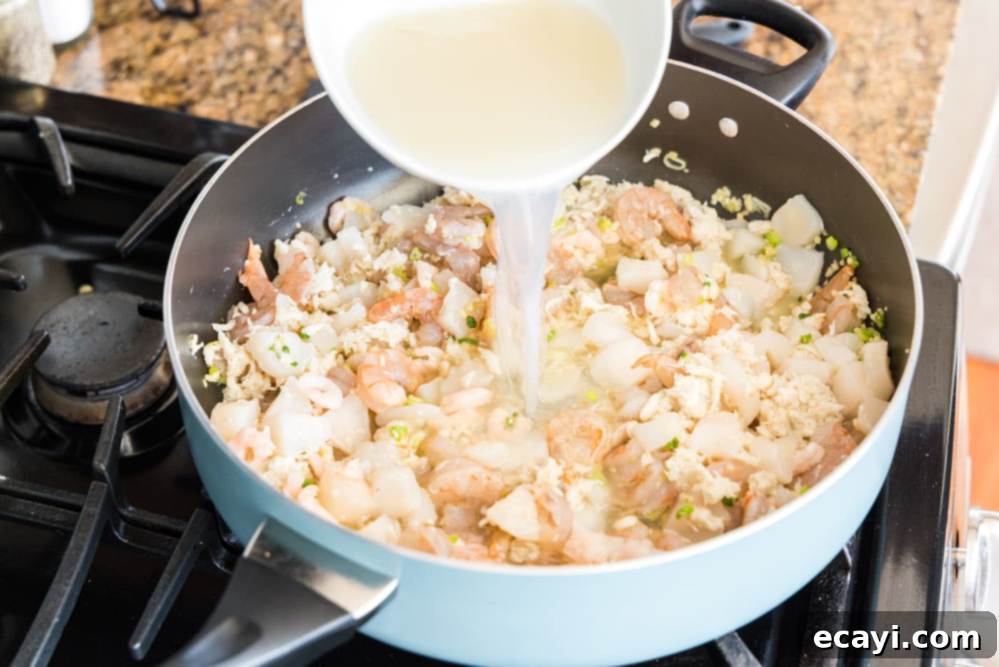 Ocean's Bounty Lasagna 7 Pouring chicken stock and clam juice over seafood mixture in a skillet.