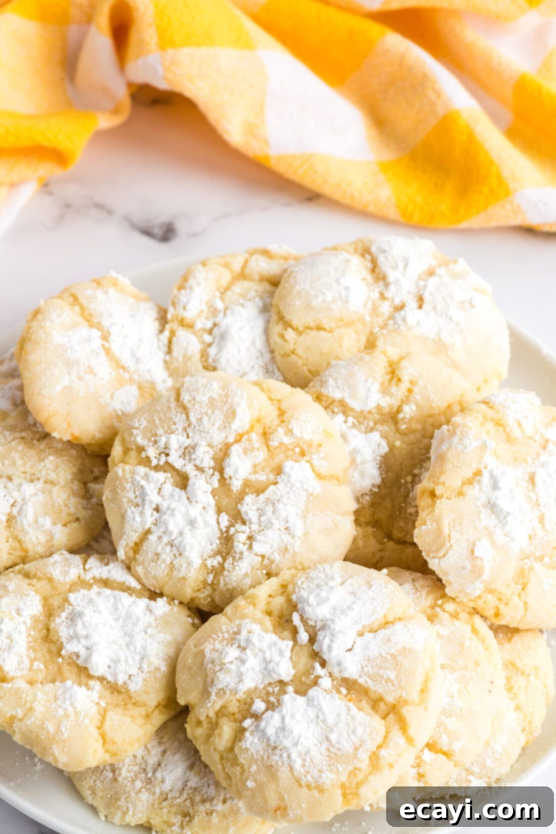 Soft and chewy Orange Crinkle Cookies, infused with real orange zest and juice, and rolled in powdered sugar for that signature crackle. A close-up of beautifully cracked orange crinkle cookies on a white plate, dusted with powdered sugar.