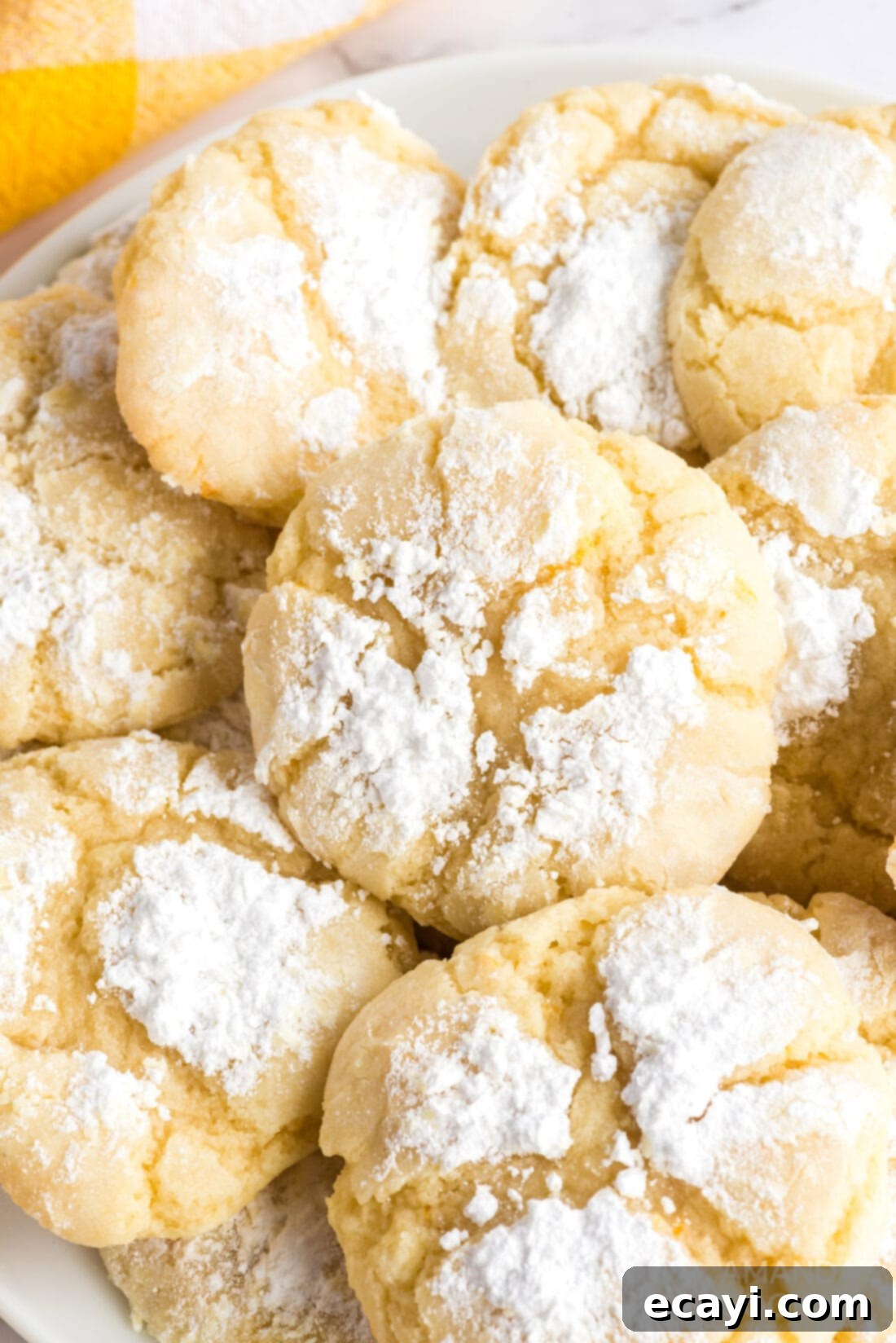 Serve up these irresistible Orange Crinkle Cookies, soft, chewy, and bursting with zesty orange flavor. A close-up shot of a plate of perfectly baked orange crinkle cookies, showing their unique powdered sugar-dusted, cracked tops.