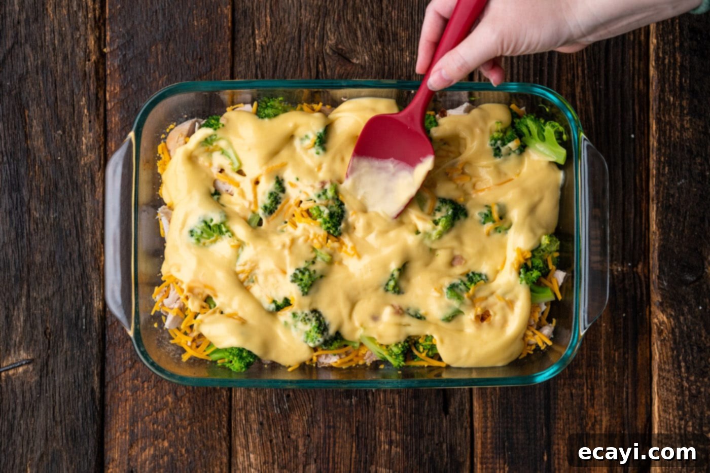 Creamy Chicken Broccoli Bake 8 spatula spreading cream of chicken over broccoli, chicken, and cheese