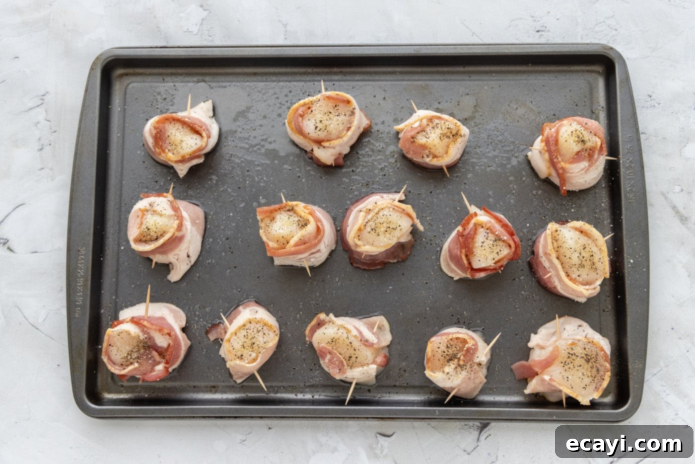 Sea Scallops Draped in Bacon 6 seasoned bacon wrapped scallops on a baking sheet