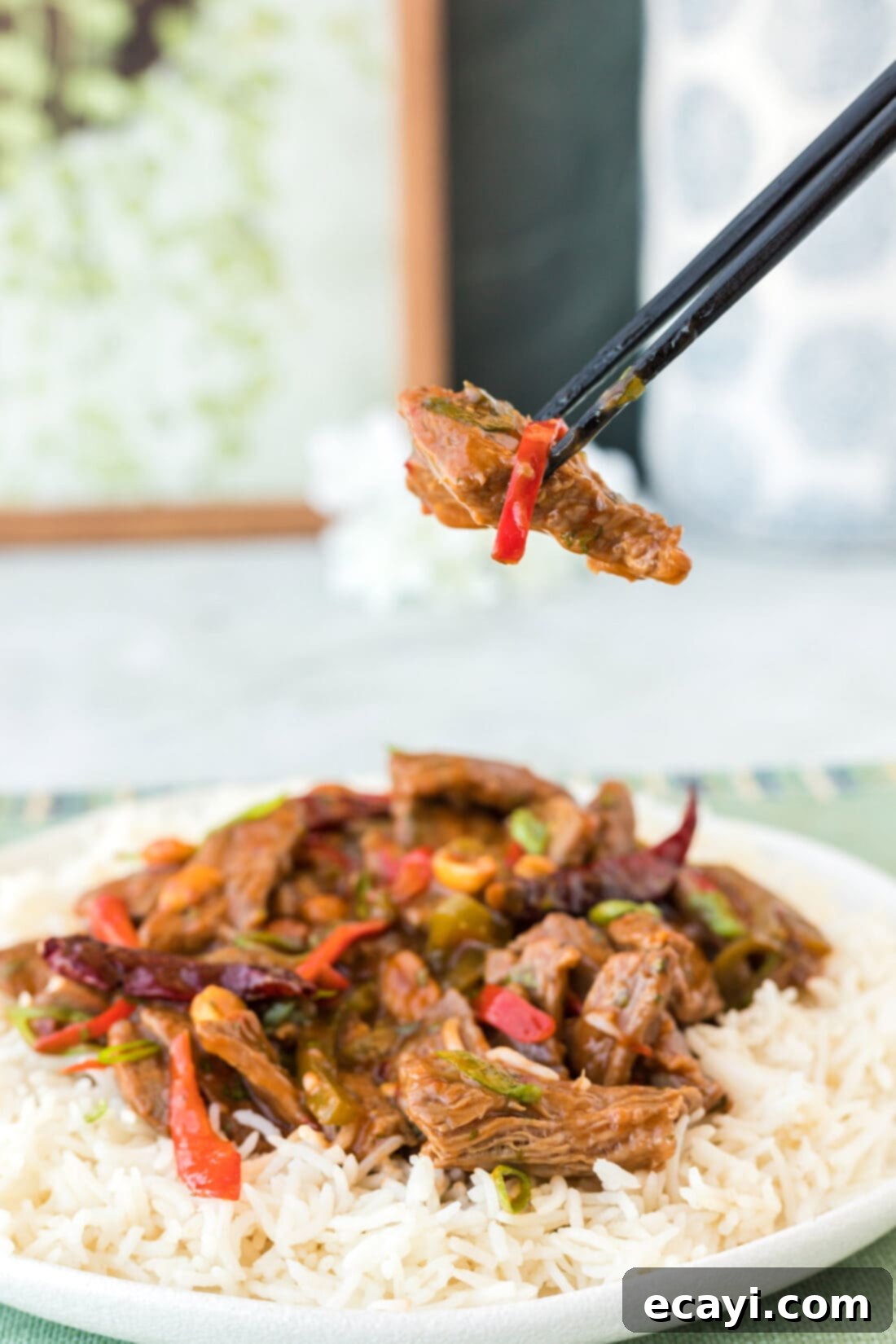Fiery Szechuan Beef 3 Close-up of chopsticks lifting a piece of Kung Pao Beef from a wok