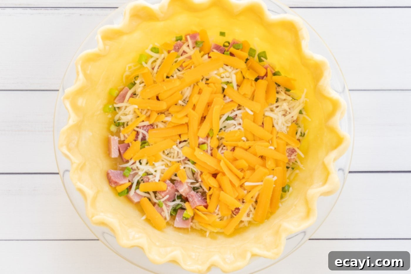 Savory Egg Custard Pie 7 Shredded cheddar cheese sprinkled over mozzarella, ham, and green onions in the pie crust.
