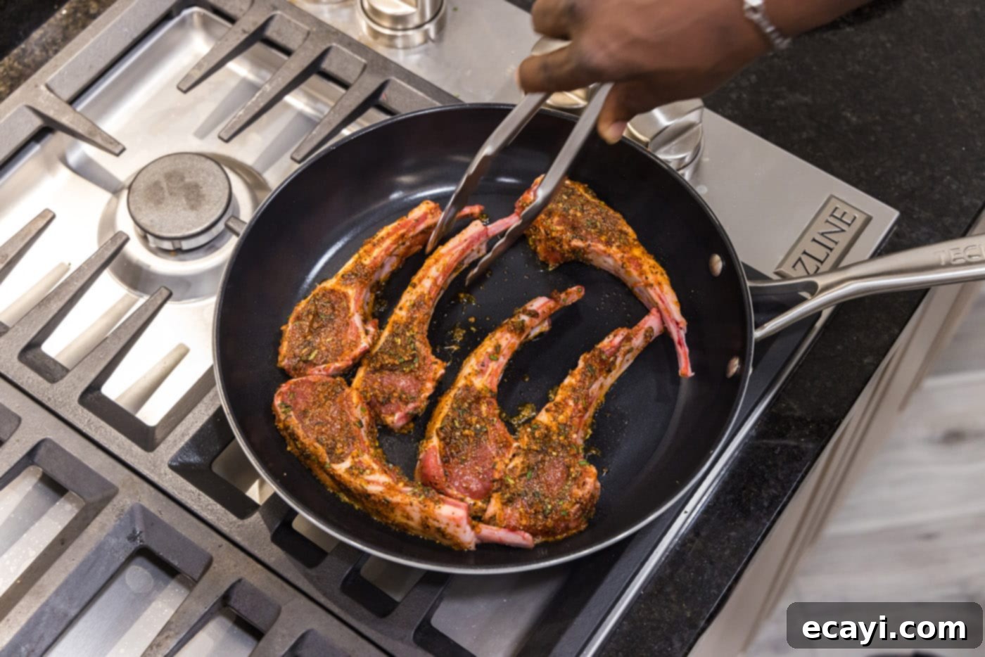 Tender Oven-Baked Lamb Chops 8 Tongs carefully placing a seasoned lamb chop into a hot oven-safe skillet on the stovetop.