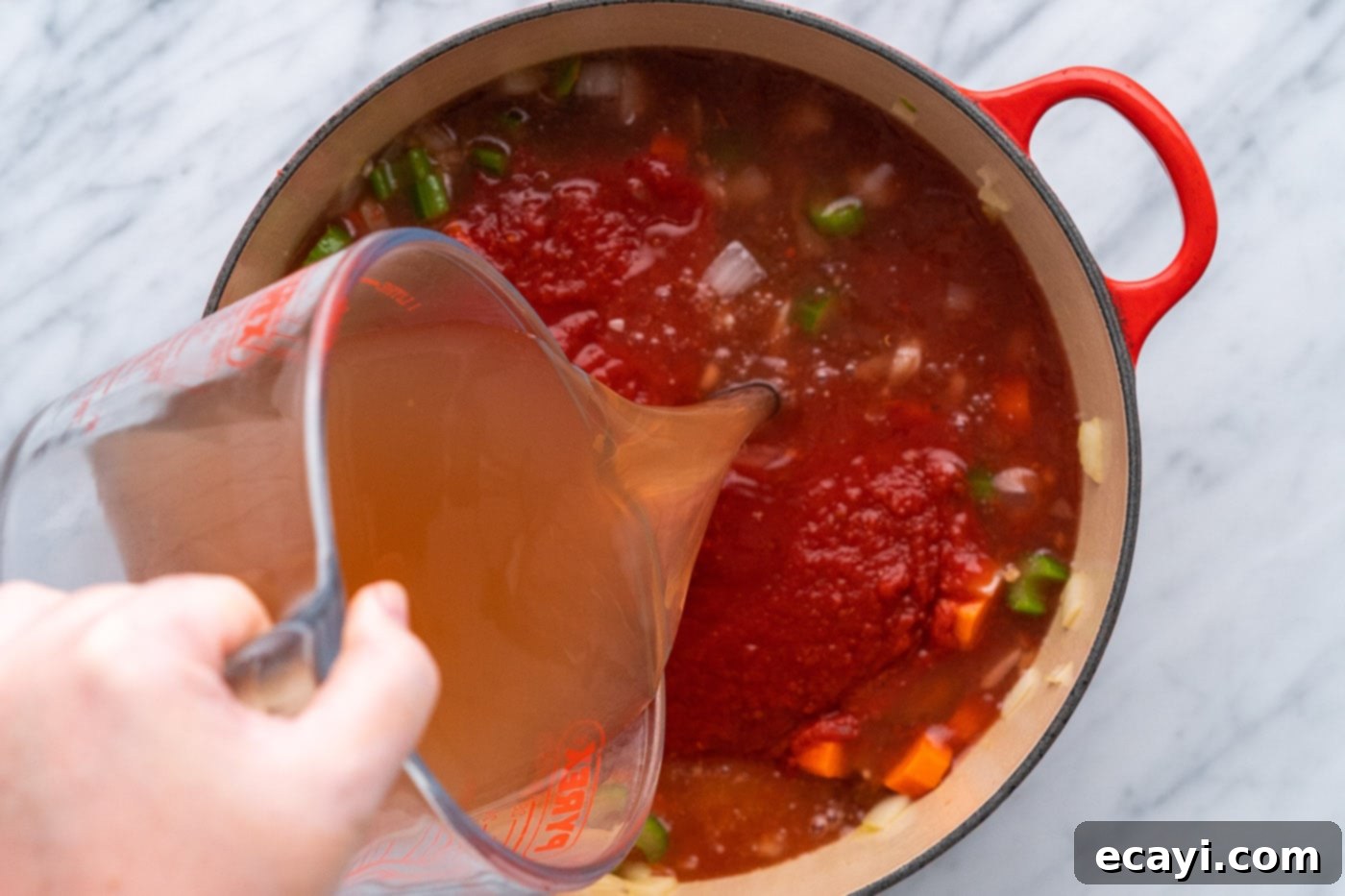 Soul-Warming Lentil Soup 8 Pouring rich vegetable broth over a medley of crushed tomatoes, sautéed celery, onion, and carrots in a pot, forming the soup base.