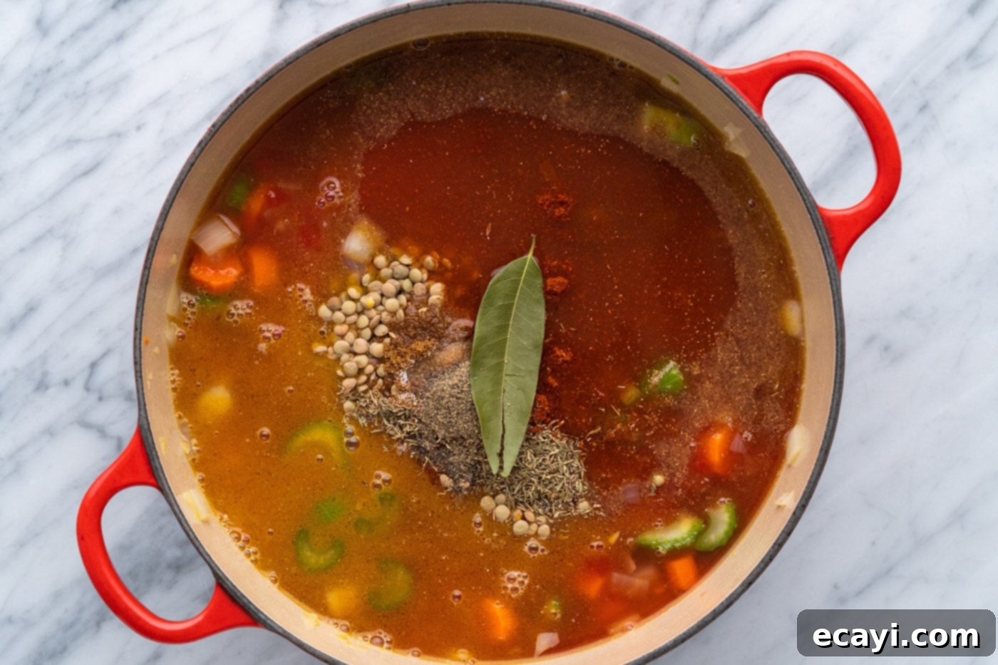 Soul-Warming Lentil Soup 9 A vibrant array of seasonings, including dried thyme, cumin, coriander, sweet paprika, and a bay leaf, sprinkled on top of lentil soup in a pot.