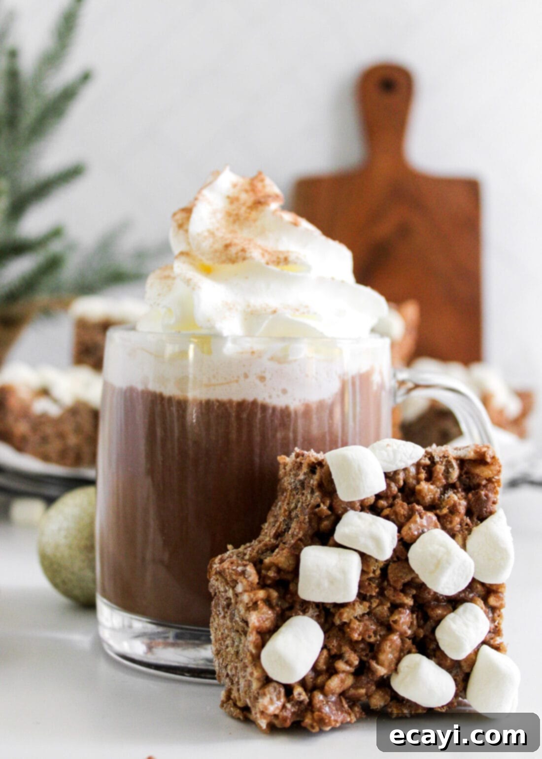Cozy Cocoa Krispie Squares 2 Hot Cocoa Rice Krispie Treats leaning against a mug of cocoa, showcasing their chewy texture and delightful hot chocolate flavor