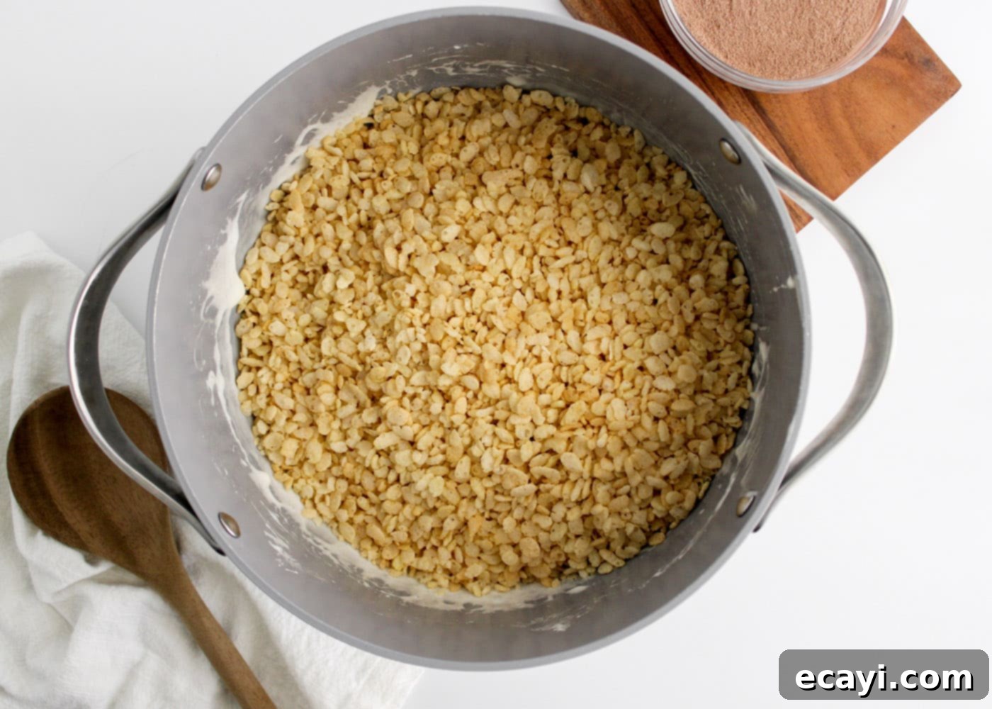 Cozy Cocoa Krispie Squares 7 adding rice krispie cereal to the marshmallow mixture in a saucepan