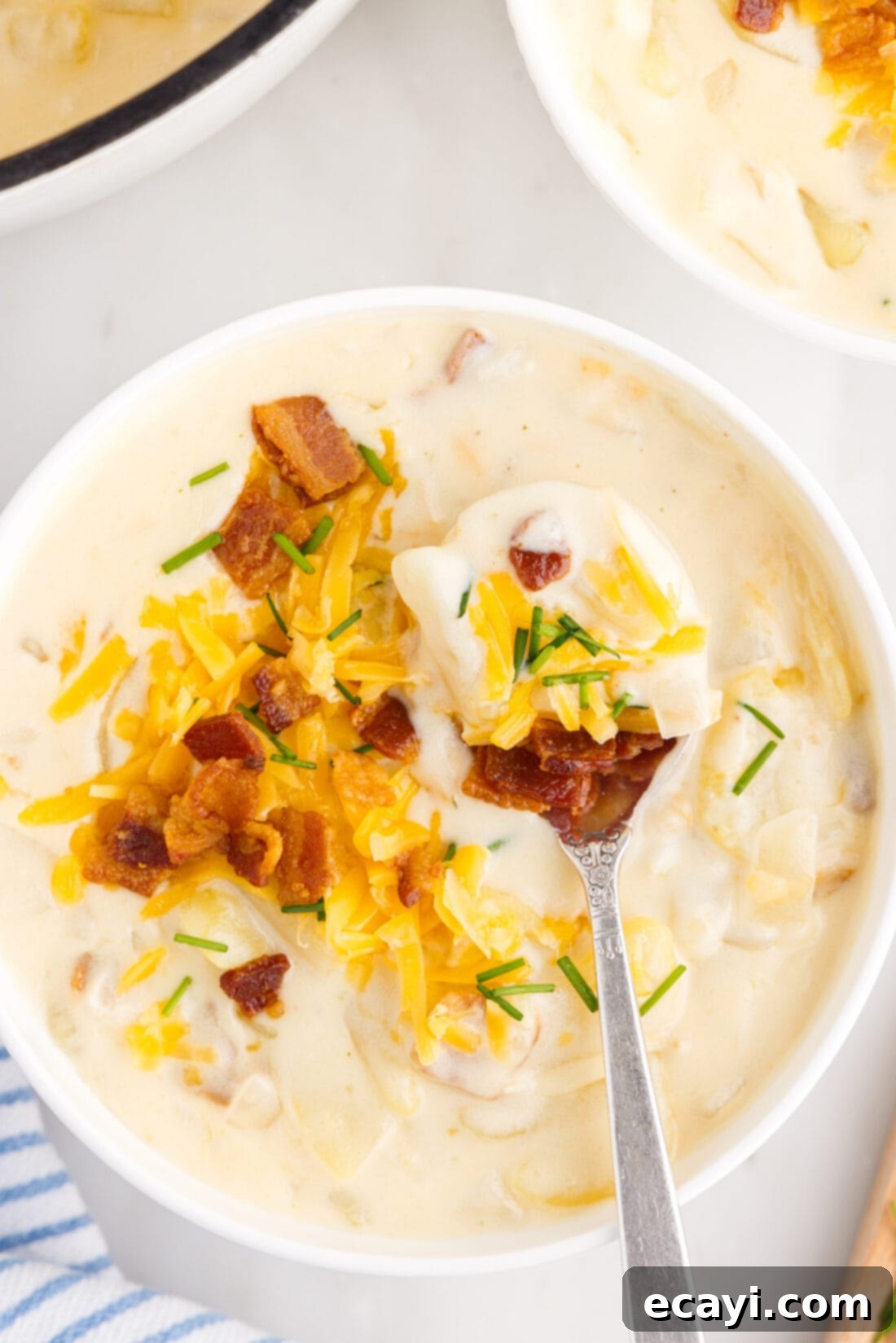 Loaded Baked Potato Soup 2 Spoonful of creamy baked potato soup garnished with bacon, cheese, and chives, lifted from a full bowl, highlighting its rich texture