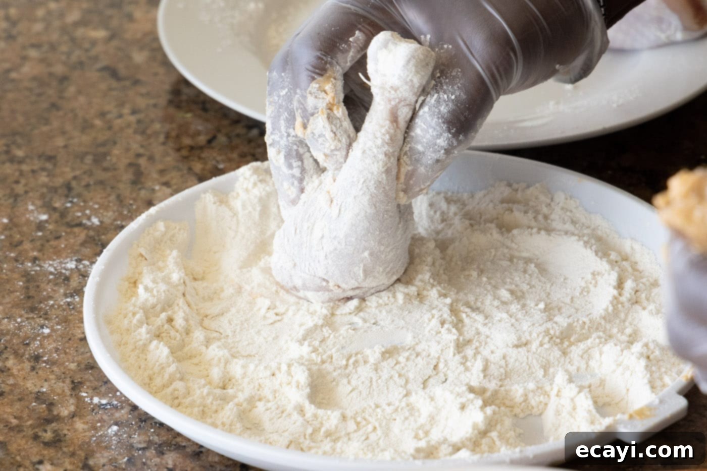 Nashville Hot Chicken 6 A hand coating chicken legs generously in flour, preparing for deep frying to make Nashville Hot Chicken.