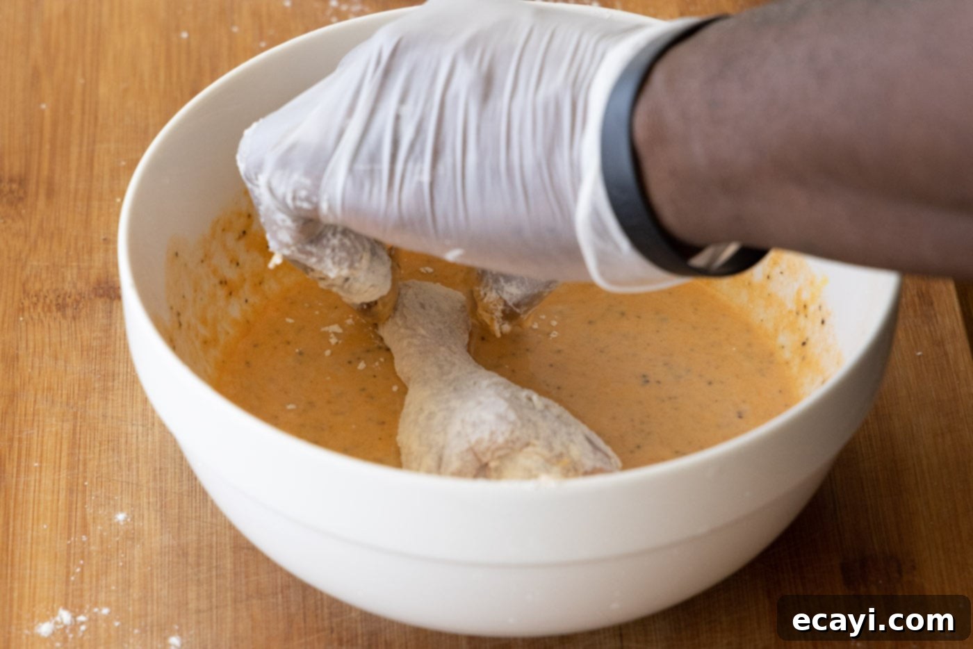 Nashville Hot Chicken 7 Chicken legs being dipped into a spiced egg mixture, ready for the next layer of breading for Nashville Hot Chicken.