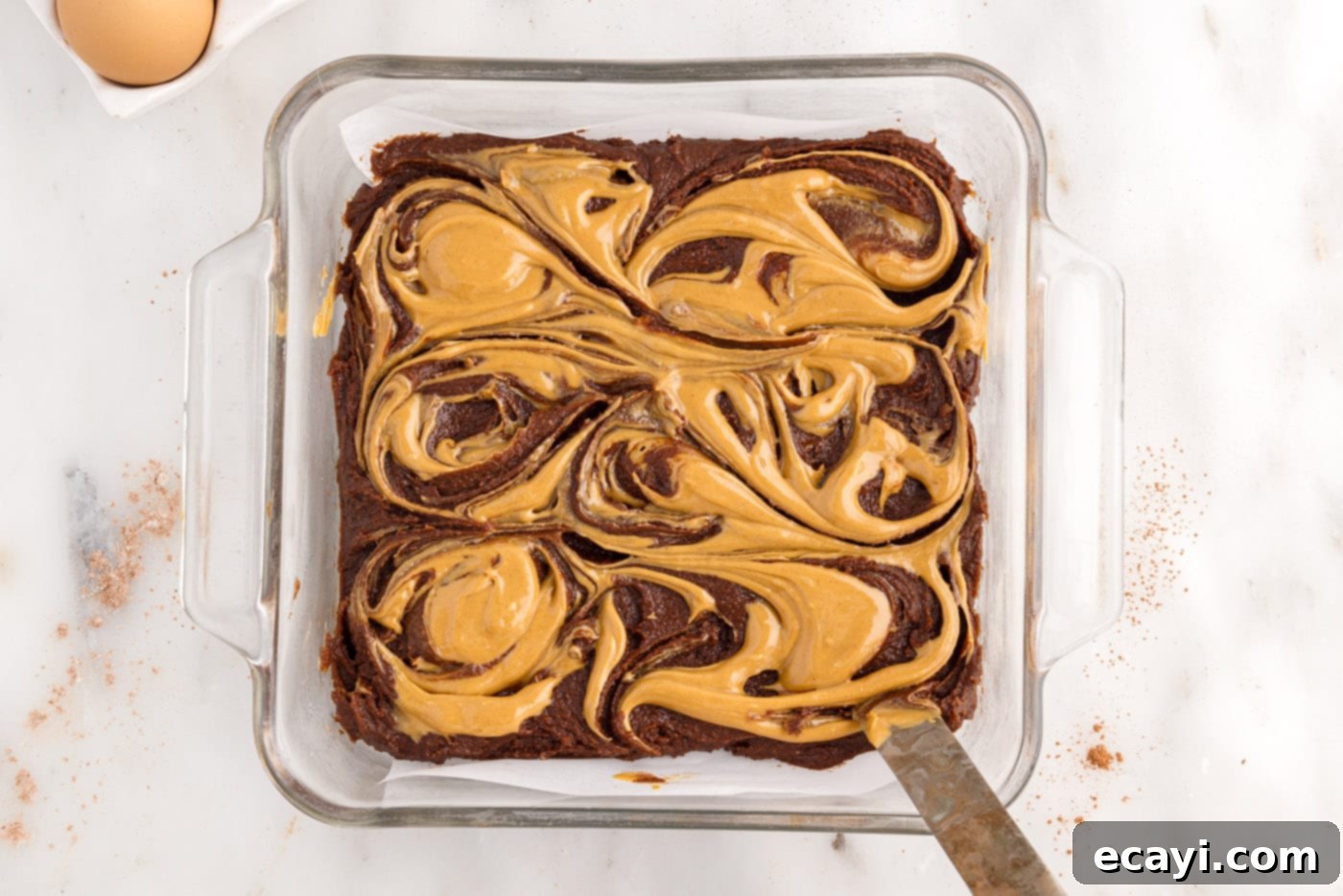 Peanut Butter Brownie Bliss 13 butter knife swirling peanut butter on top of brownie batter in a pan
